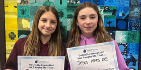 Two students holding signs that share what Catholic Education has taught them.